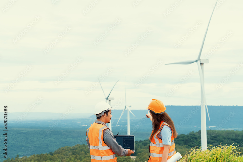 Male and female engineers working on a wind farm atop a hill or mountain in the rural. Progressive i