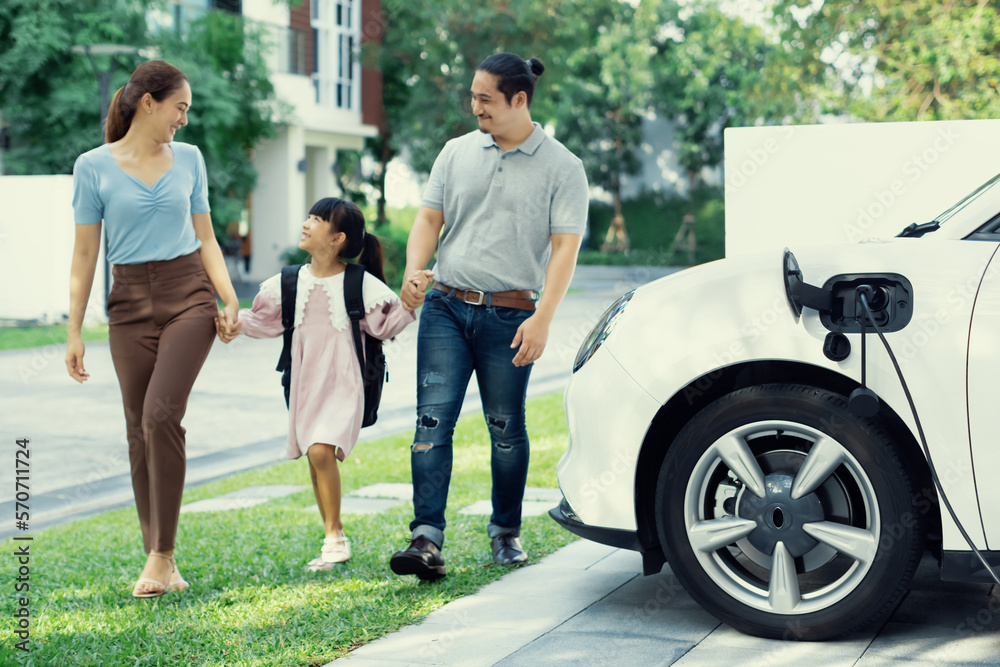 Progressive young happy family with electric vehicle and home backyard charging station. Green and c