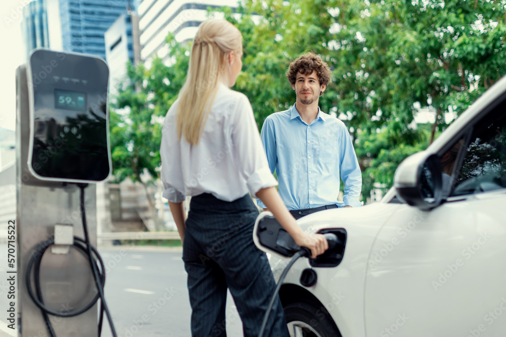 Progressive businessman and businesswoman with electric car parking and connected to public charging