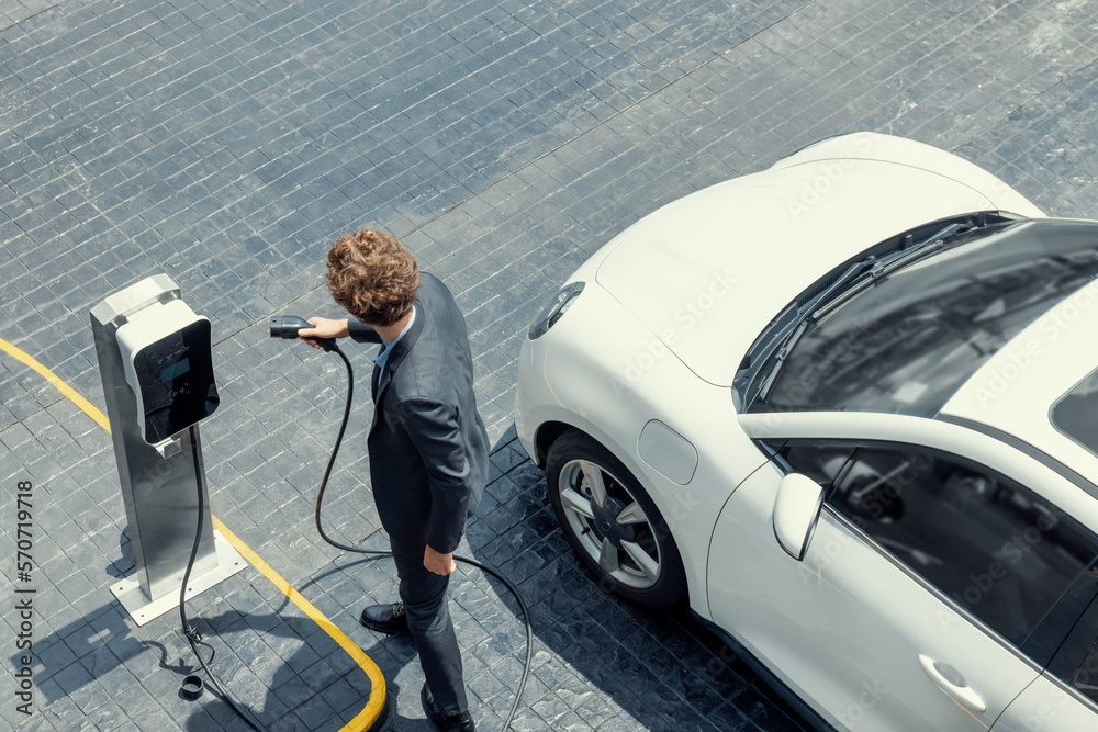 Aerial view of progressive businessman in black formal suit with his electric vehicle recharging bat