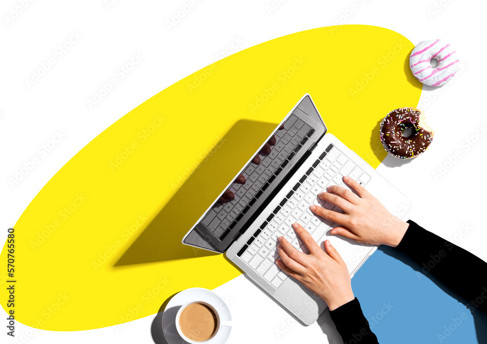 Person using a laptop computer with a donut and a cup of coffee - Flat lay