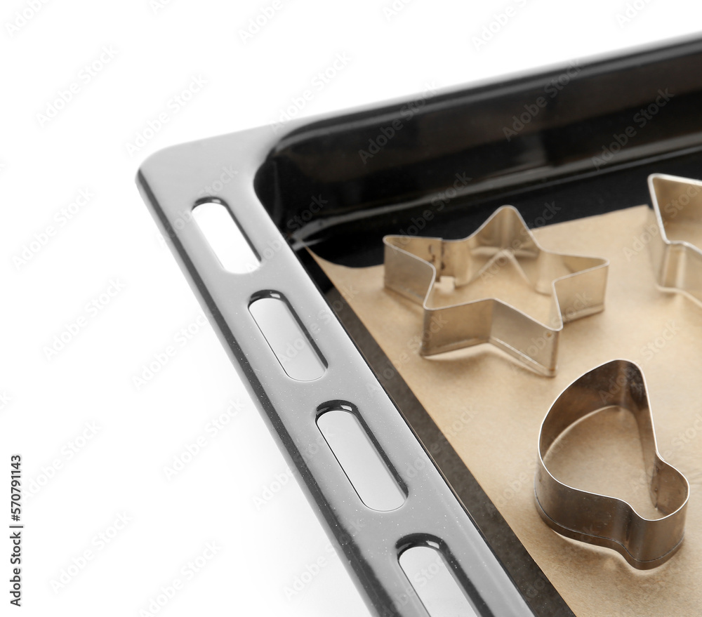 Baking sheet with paper and cookie cutters on white background, closeup