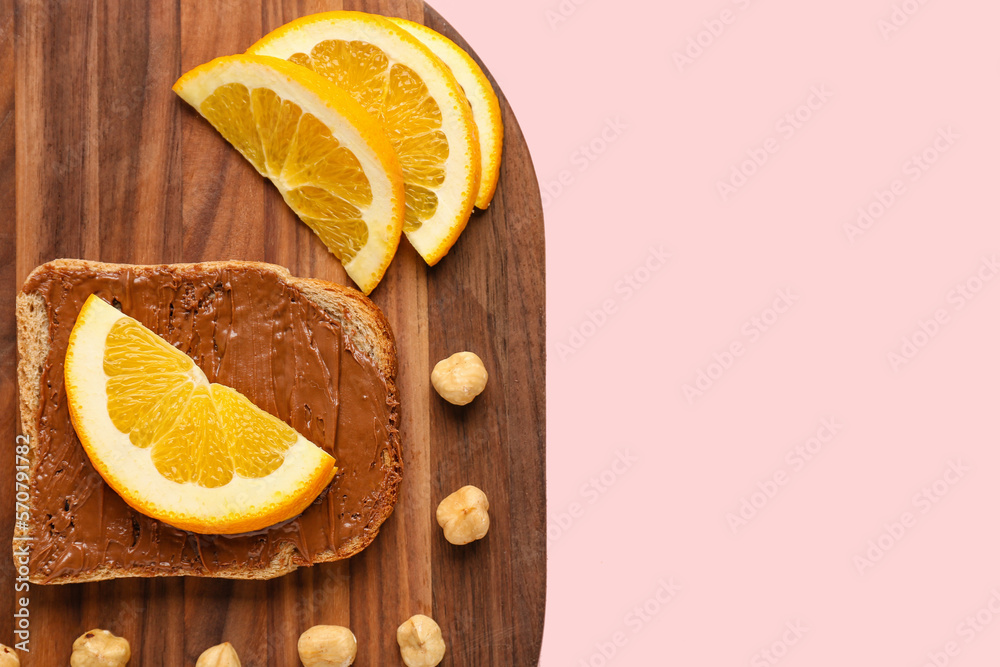 Wooden board of tasty toast with hazelnut butter and orange slices on pink background, closeup