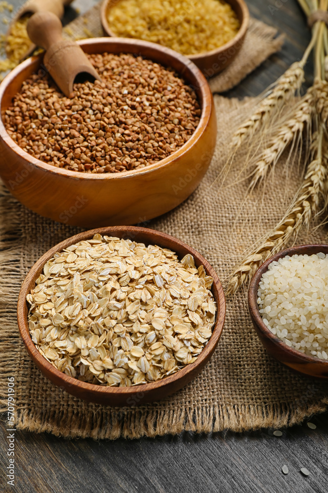 Bowls with different cereals on dark wooden background, closeup