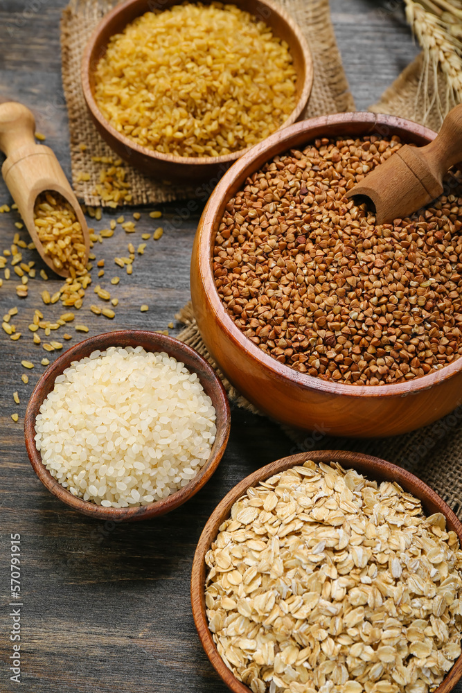 Bowls with different cereals on dark wooden background, closeup