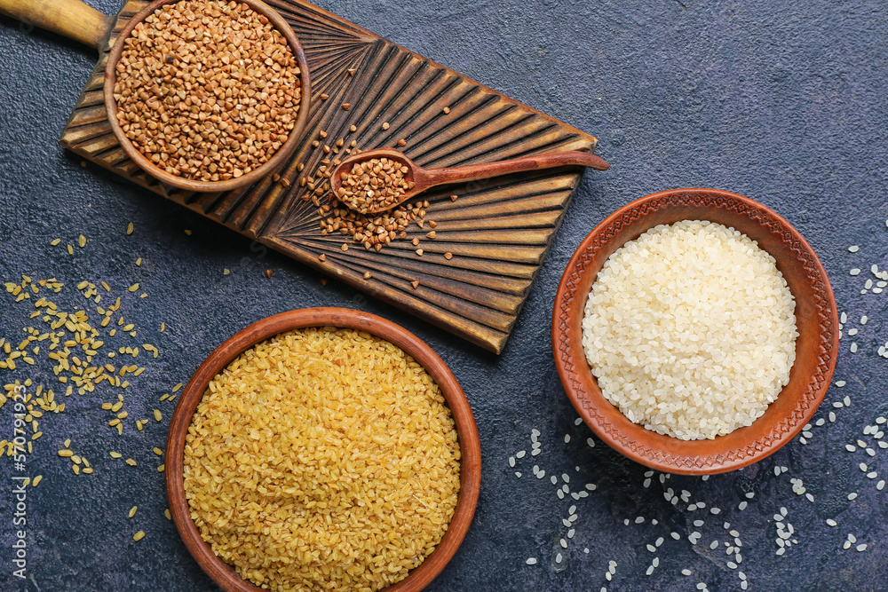 Bowls with buckwheat, rice and bulgur on dark background