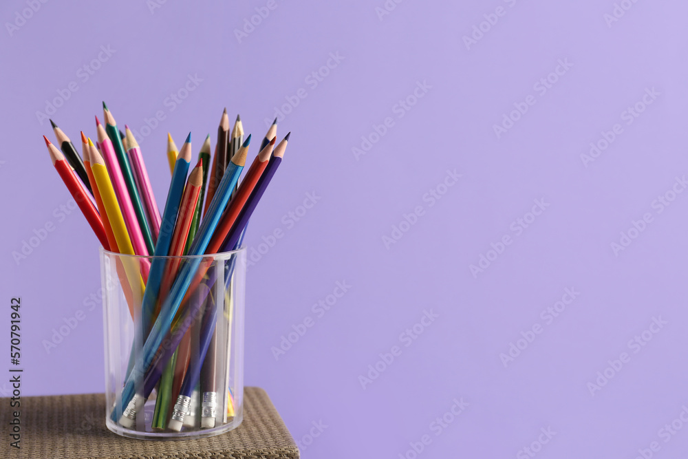 Glass of colorful pencils on lilac background