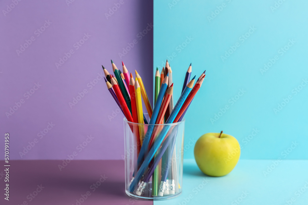 Glass of colorful pencils and apple on color background