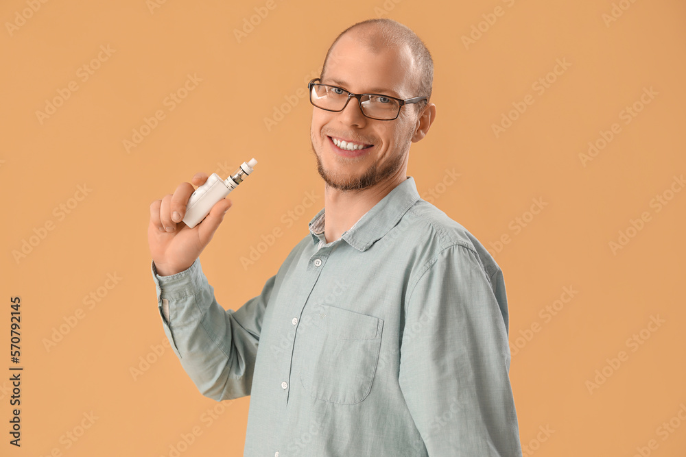 Young man in eyeglasses with disposable electronic cigarette on beige background