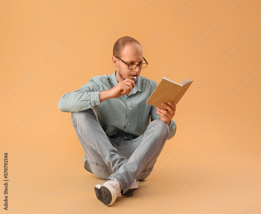 Young man in eyeglasses with disposable electronic cigarette reading book on beige background