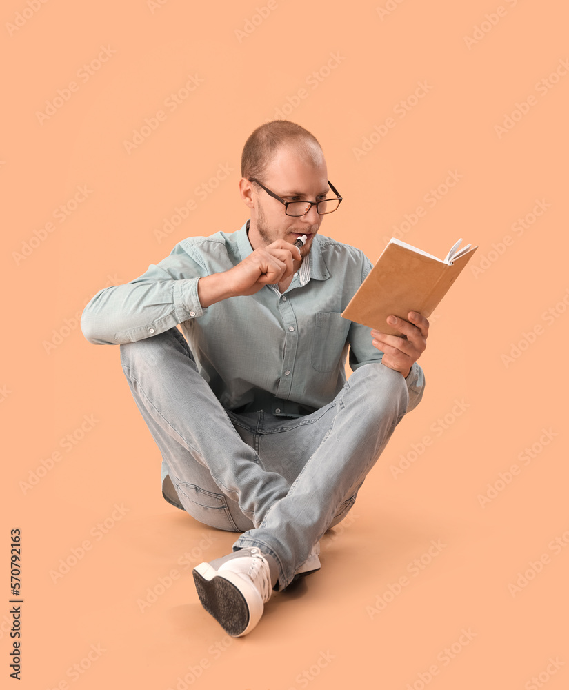 Young man in eyeglasses with disposable electronic cigarette reading book on beige background