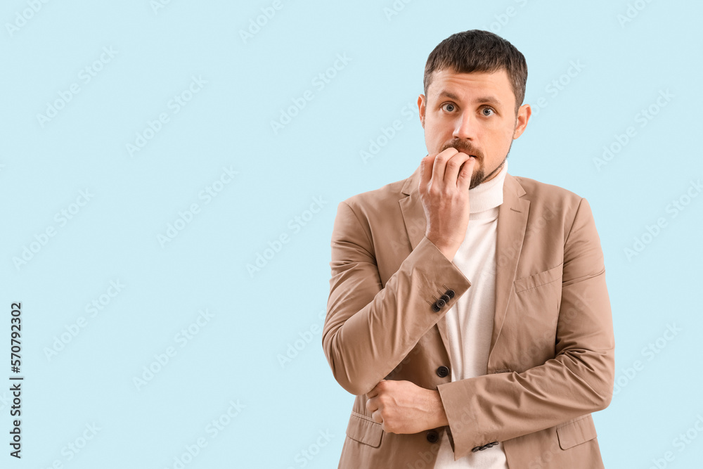 Handsome businessman biting nails on blue background