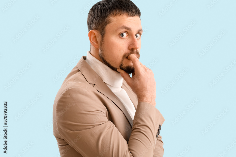 Handsome businessman biting nails on blue background, closeup