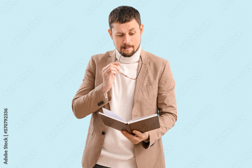 Handsome businessman with book biting eyeglasses on blue background