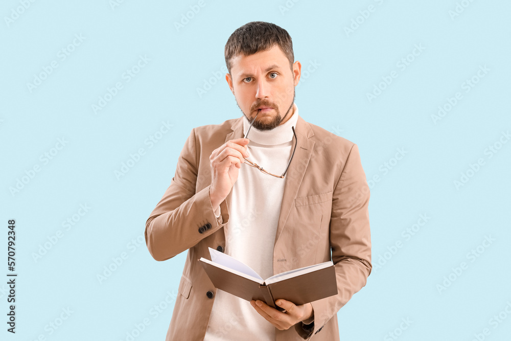 Handsome businessman with book biting eyeglasses on blue background