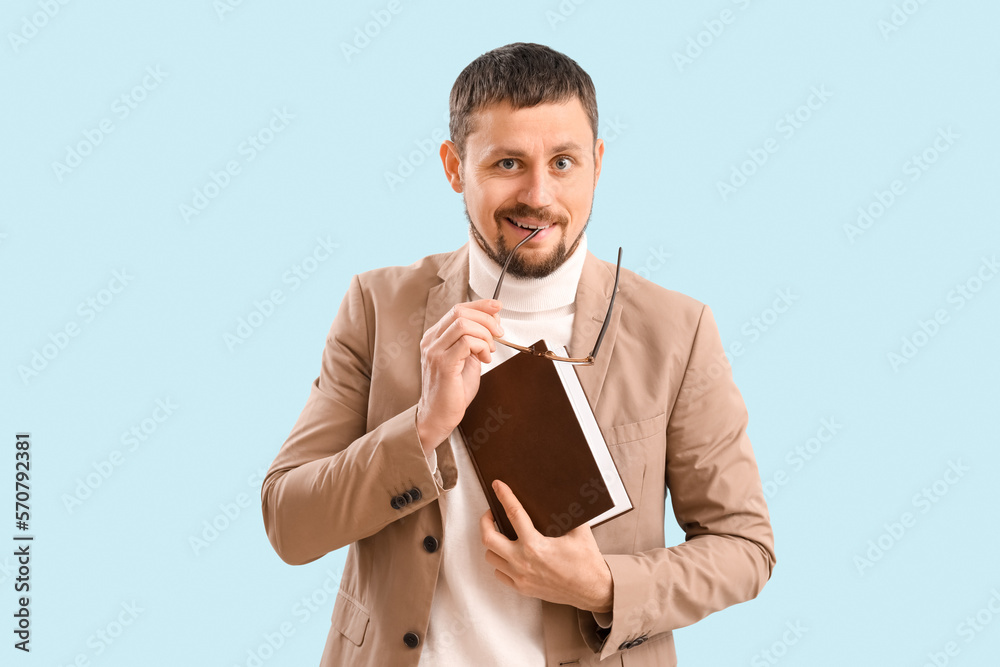 Handsome businessman with book biting eyeglasses on blue background