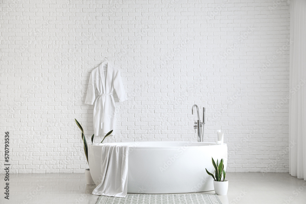 Interior of light bathroom with bathtub and houseplants