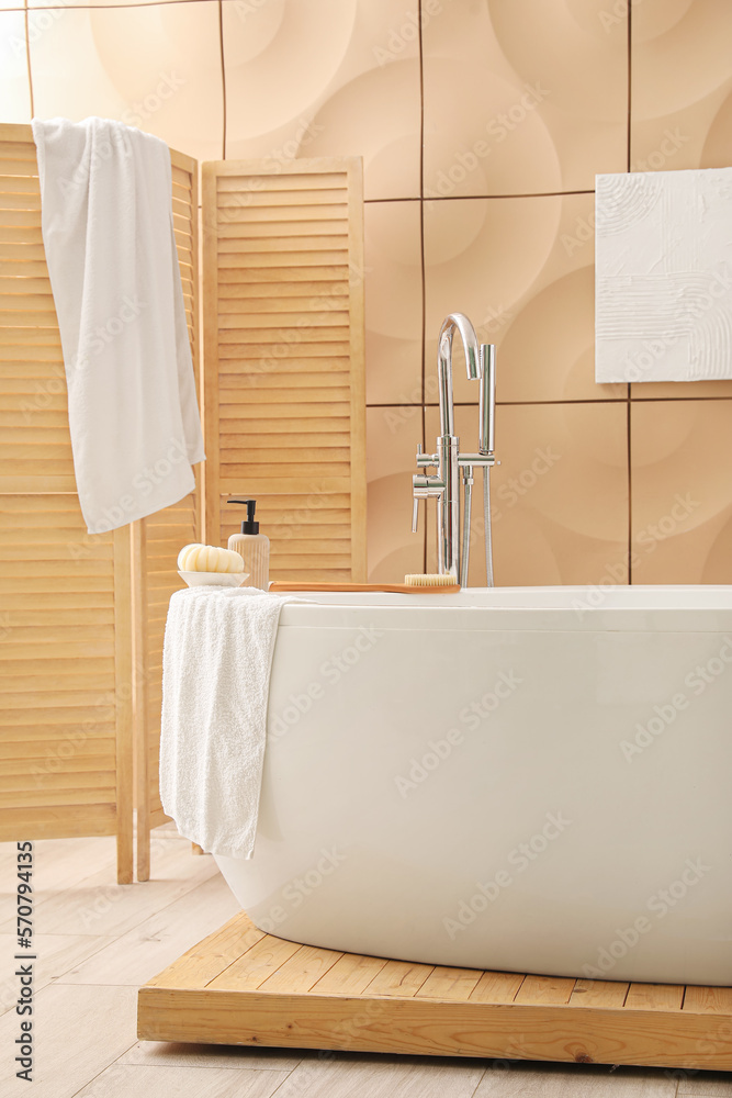 Interior of bathroom with modern bathtub, folding screen and towels