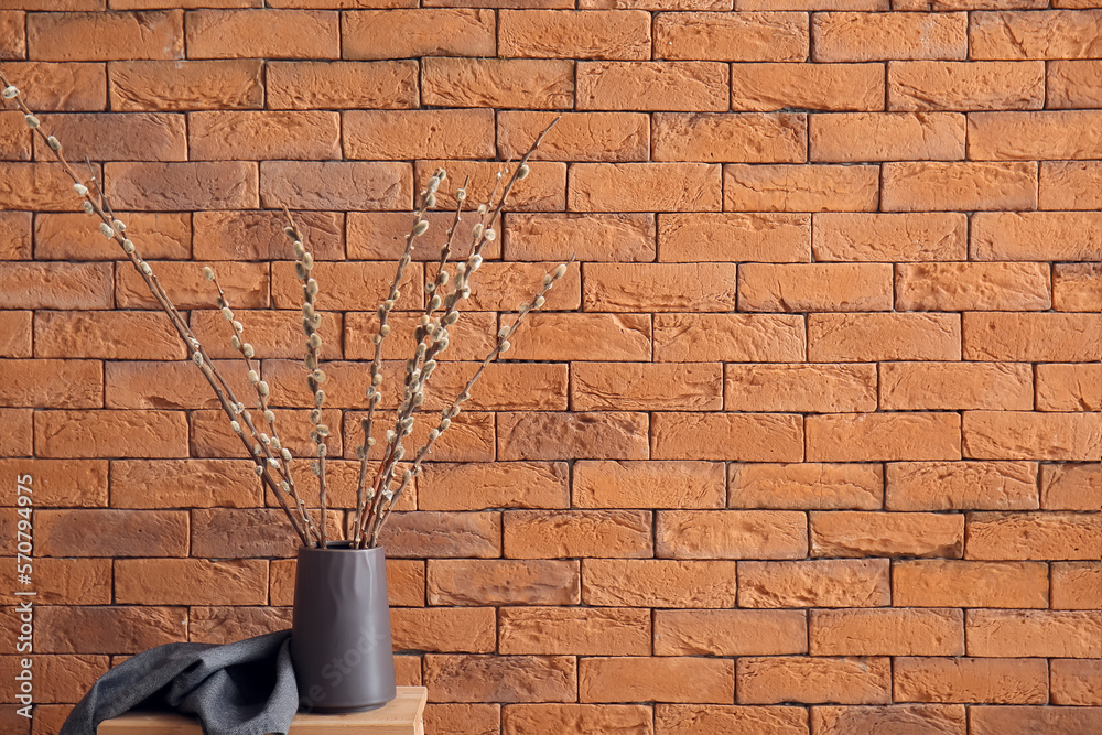 Vase with pussy willow branches on stool near brick wall