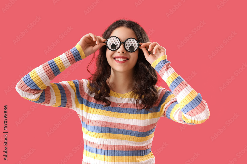 Teenage girl in funny eyeglasses on red background. April Fools Day celebration