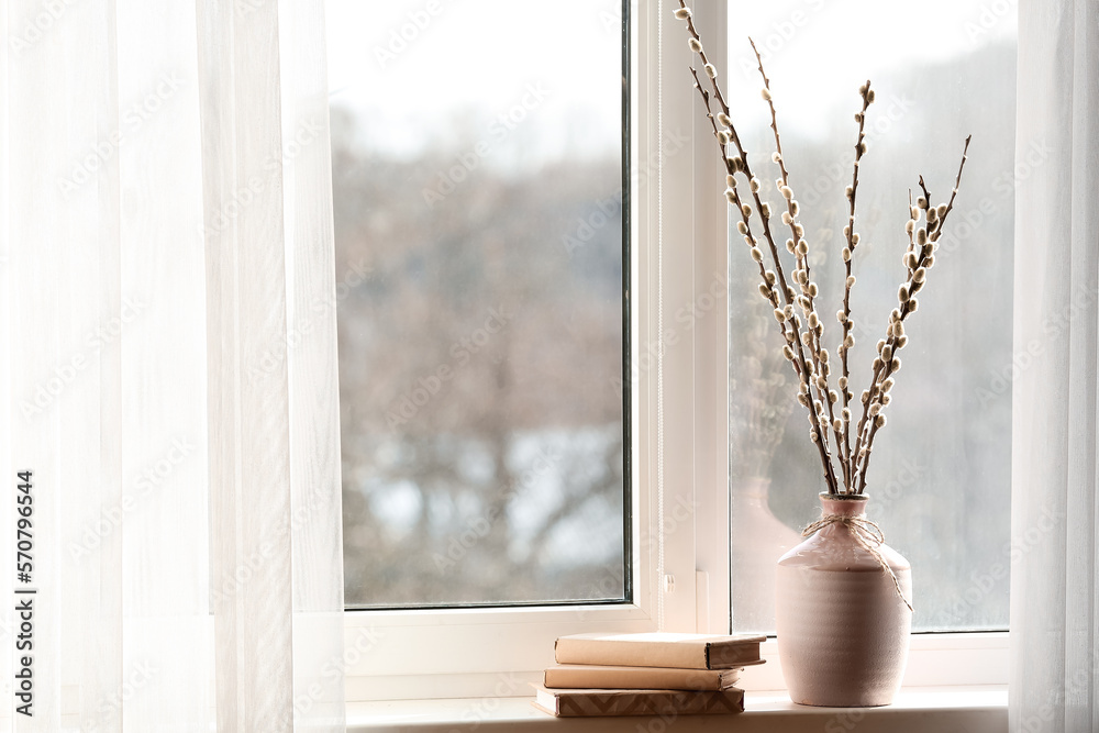 Vase with pussy willow branches and books on windowsill in room