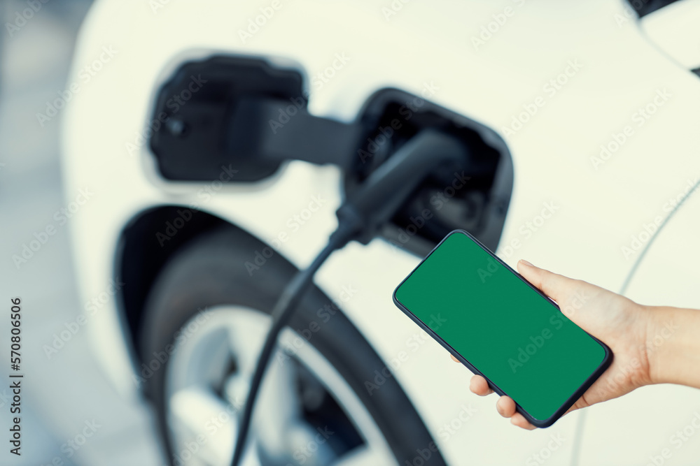 Mockup phone with green screen display energy status of electric vehicle connected to charging stati