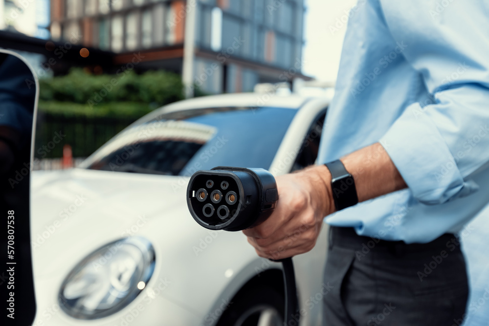 Closeup progressive man holding EV charger plug from public charging station for electric vehicle wi