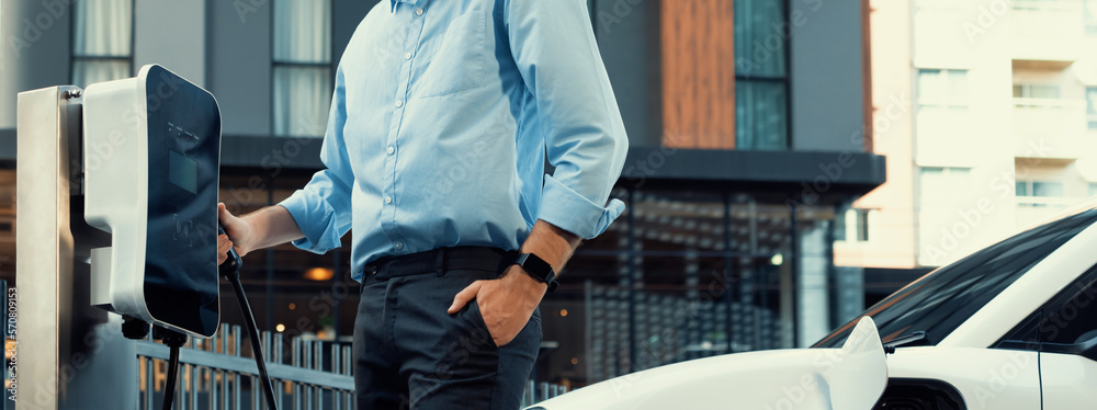 Closeup progressive man holding EV charger plug from public charging station for electric vehicle wi