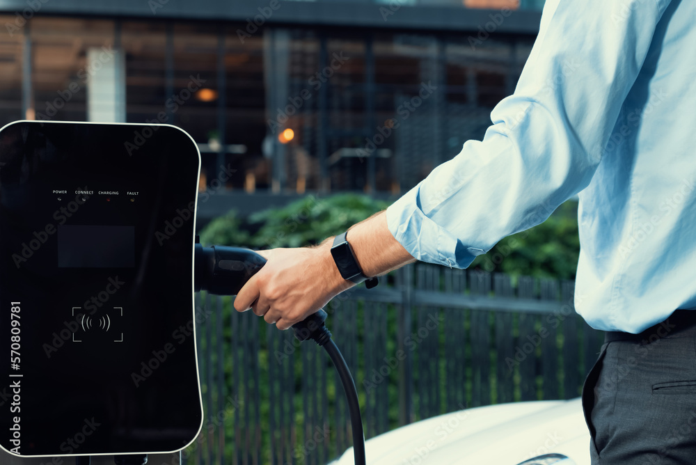 Closeup progressive man holding EV charger plug from public charging station for electric vehicle wi