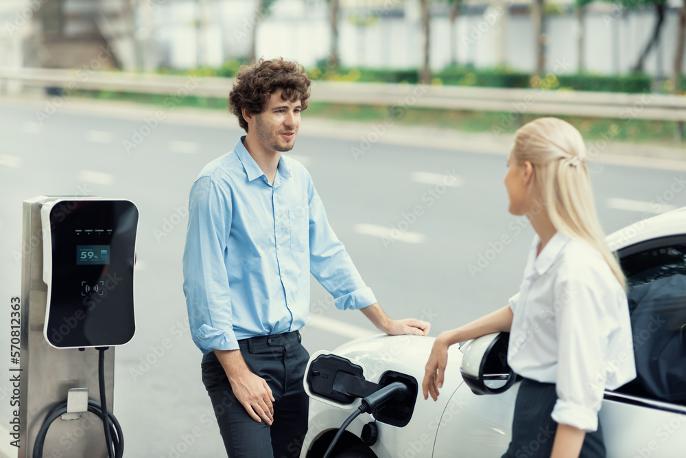 Progressive businessman and businesswoman with electric car parking and connected to public charging