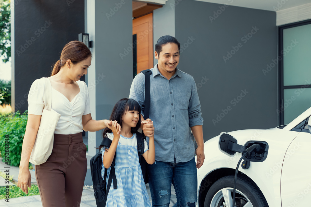 Progressive young parents and daughter with electric vehicle and home charging station. Green and cl