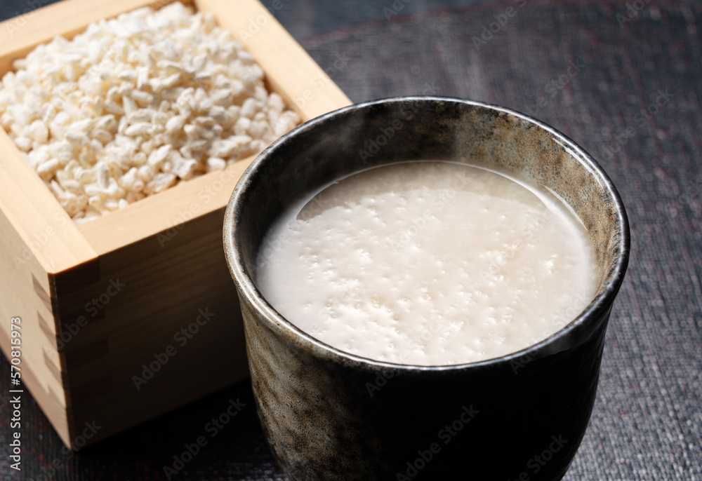 Amazake placed against a black background and rice koji in a masu box.