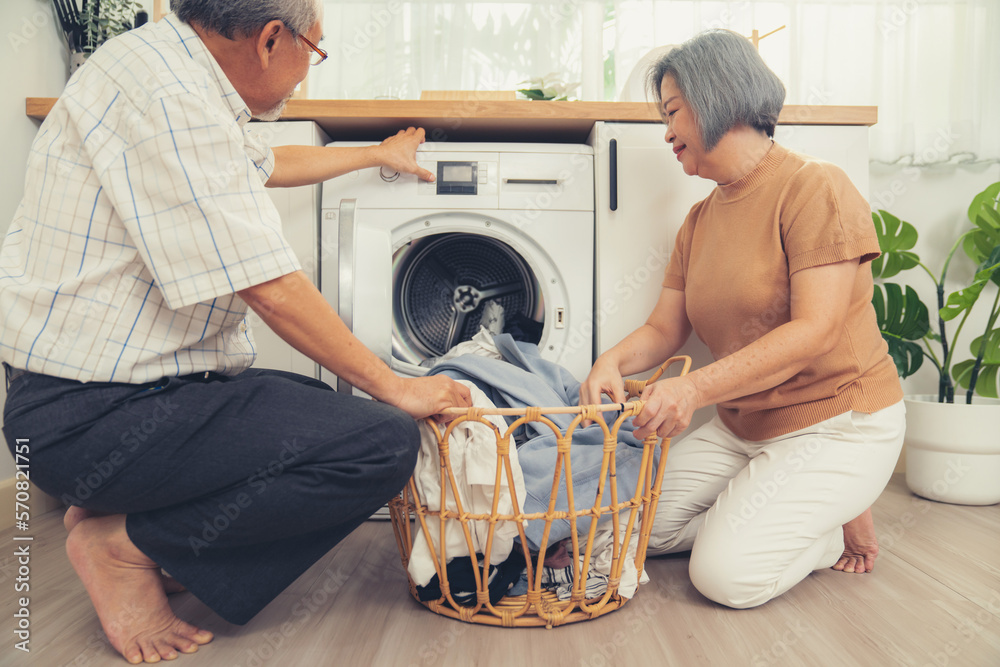 Senior couple working together to complete their household chores at the washing machine in a happy 