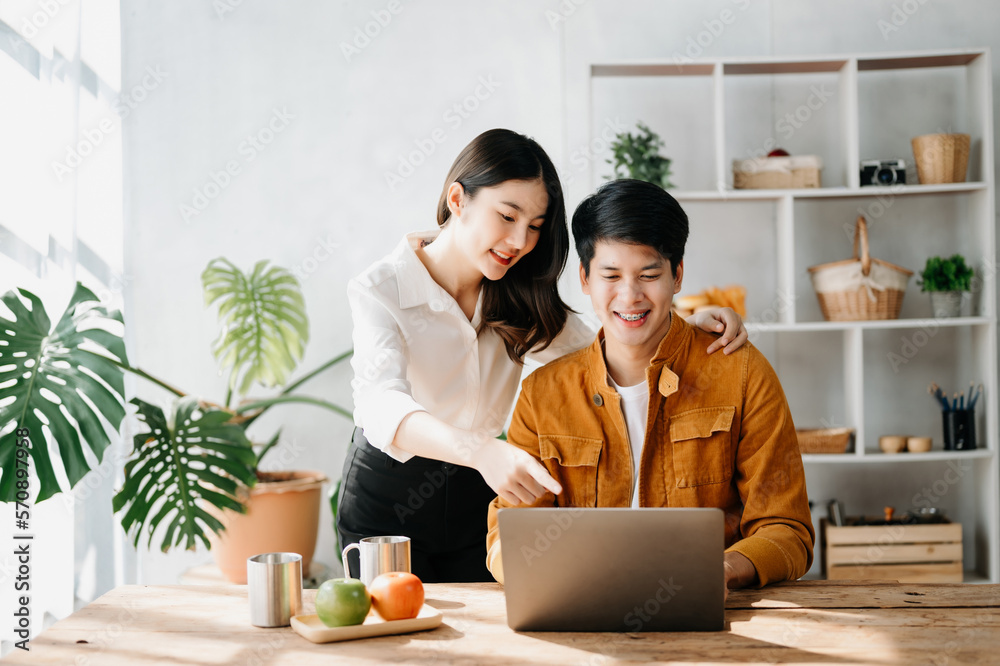 Two Asian business workers talking on the smartphone and using laptop at the home office.