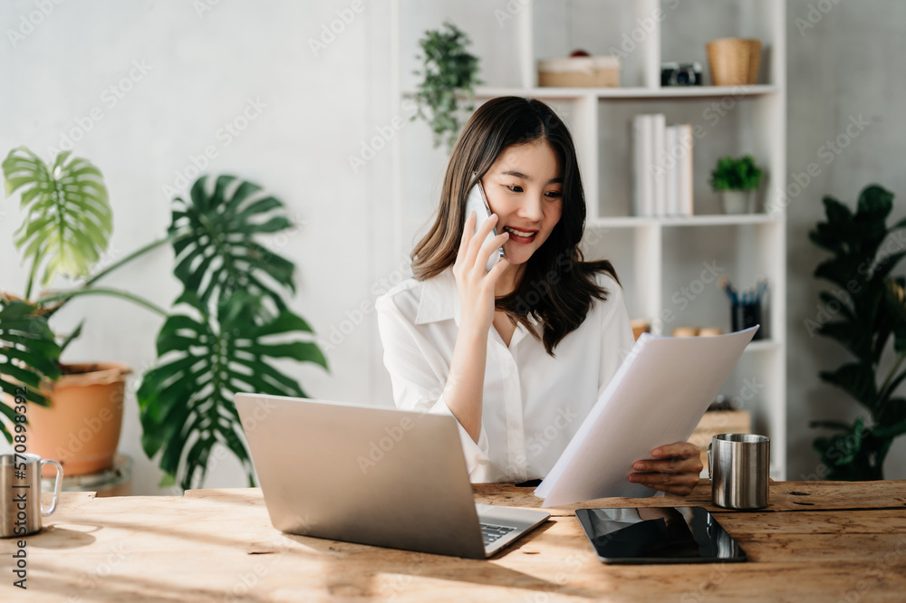 Business asian woman Talking on the phone and using a laptop with a smile while sitting at home offi