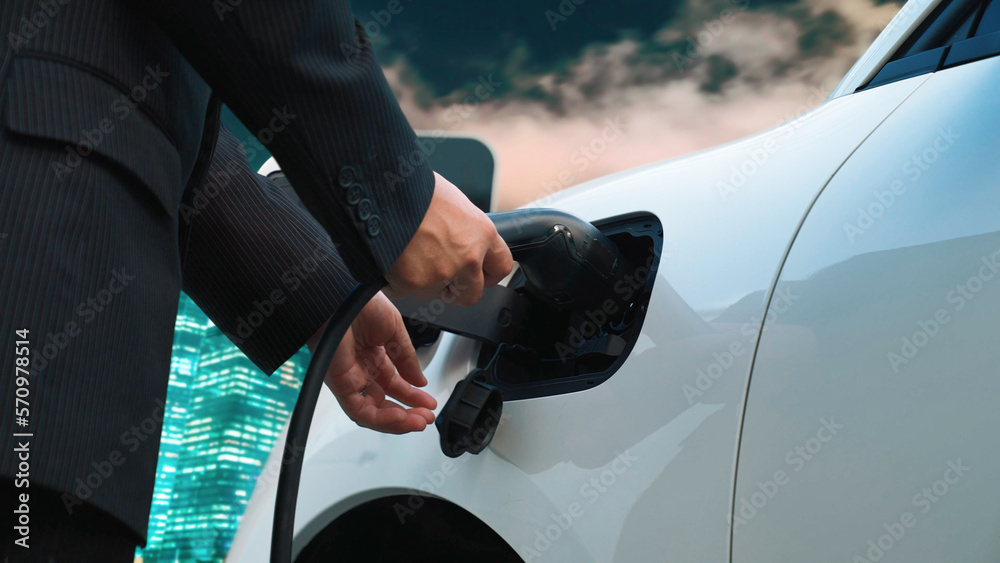 Progressive businessman recharge his electric vehicle with charger cable plug from charging station 