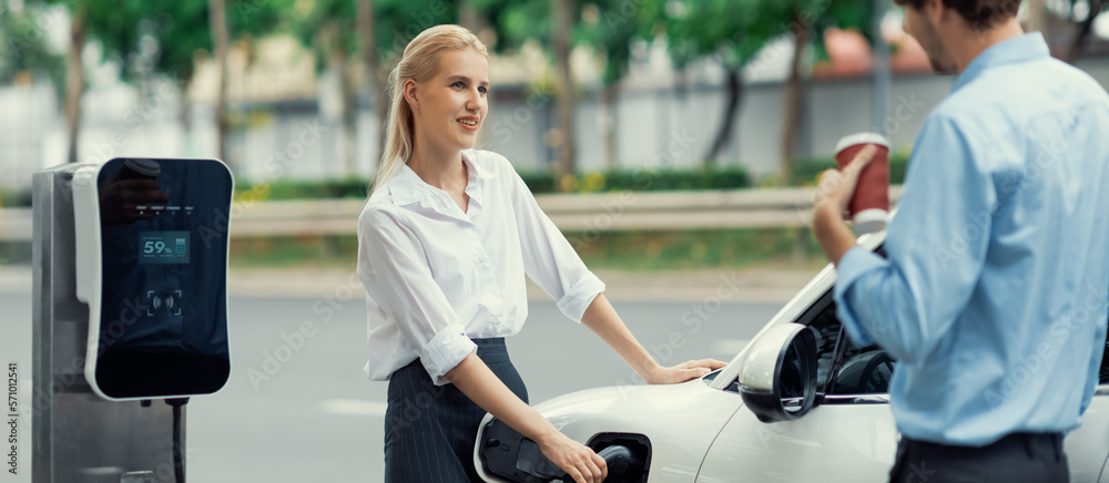 Progressive businessman and businesswoman with electric car parking and connected to public charging