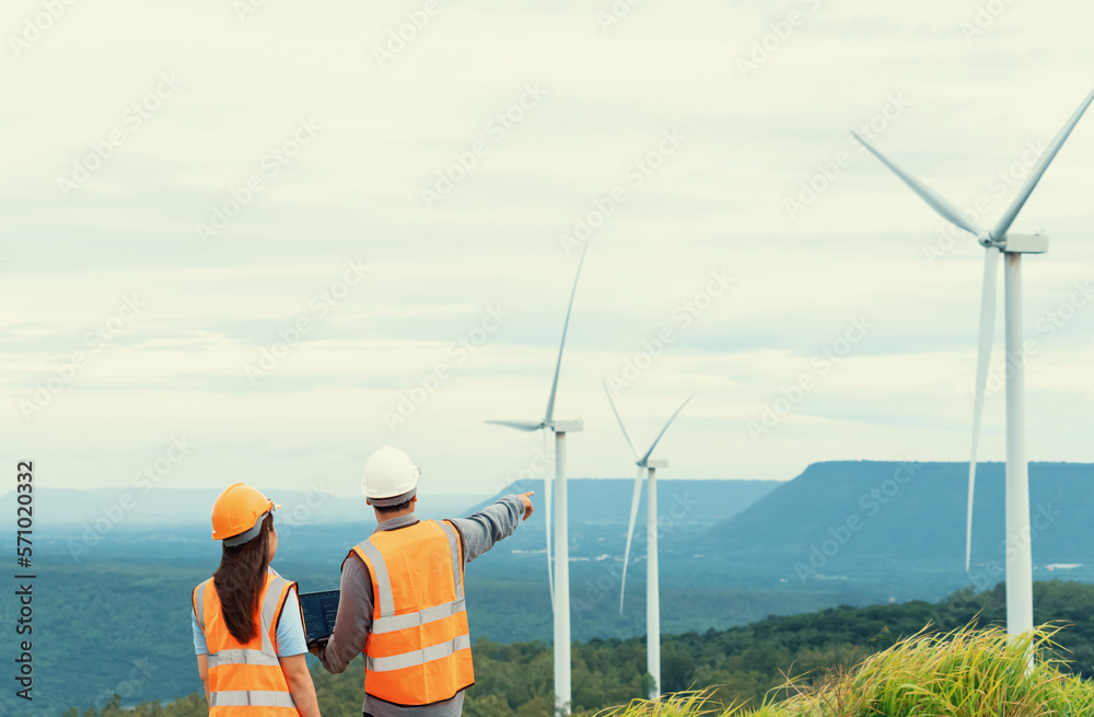 Male and female engineers working on a wind farm atop a hill or mountain in the rural. Progressive i