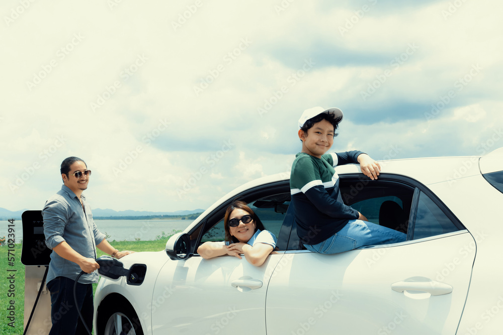 Concept of progressive happy family enjoying their time at green field and lake with electric vehicl