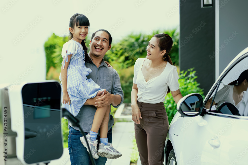 Progressive young parent teach daughter how to recharge or refuel EV car at home charging station. G