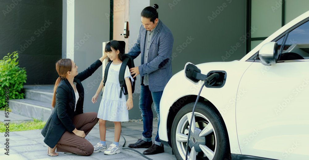 Progressive young parents and daughter with electric vehicle and home charging station. Green and cl