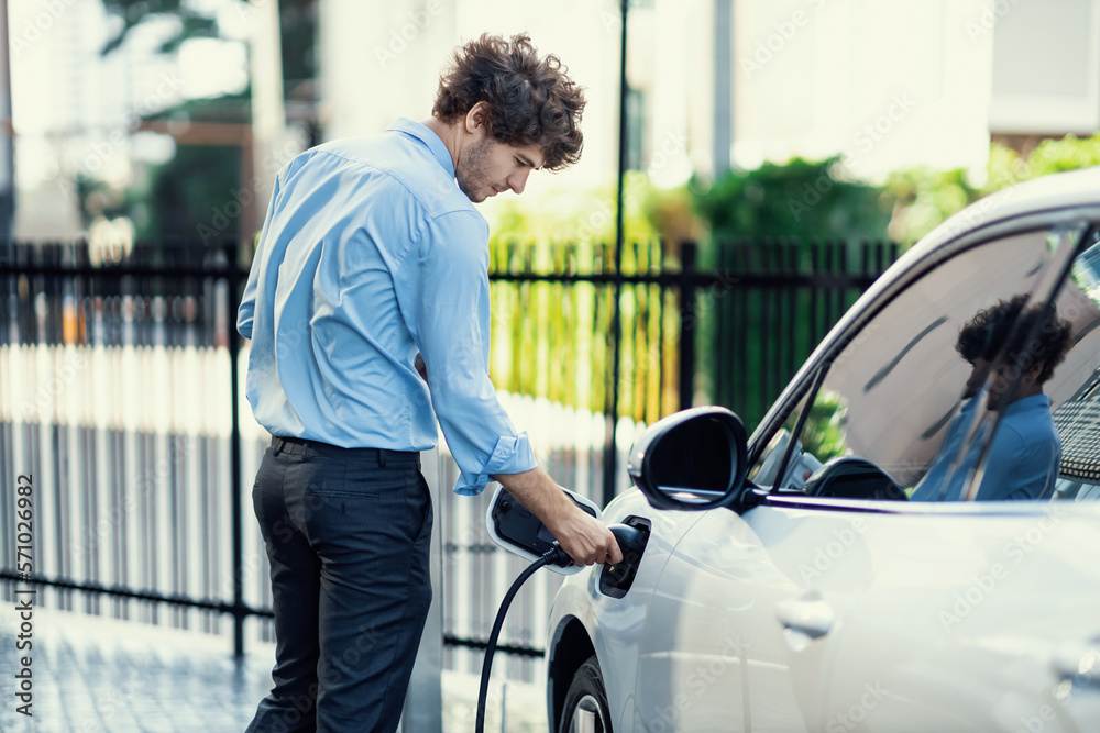 Progressive businessman insert charger plug from charging station to his electric vehicle with apart