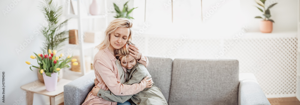 Mother and daughter sitting on the sofa indoor and embracing.