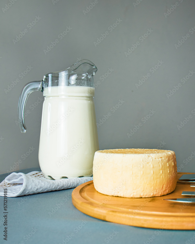 cheese caciotta on a cutting board , next to a glass jug of milk, cheese making, homemade cheese fac