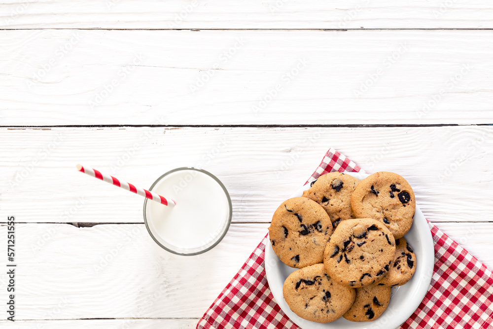 Plate with chocolate chip cookies, and a glass of milk on a wooden background.