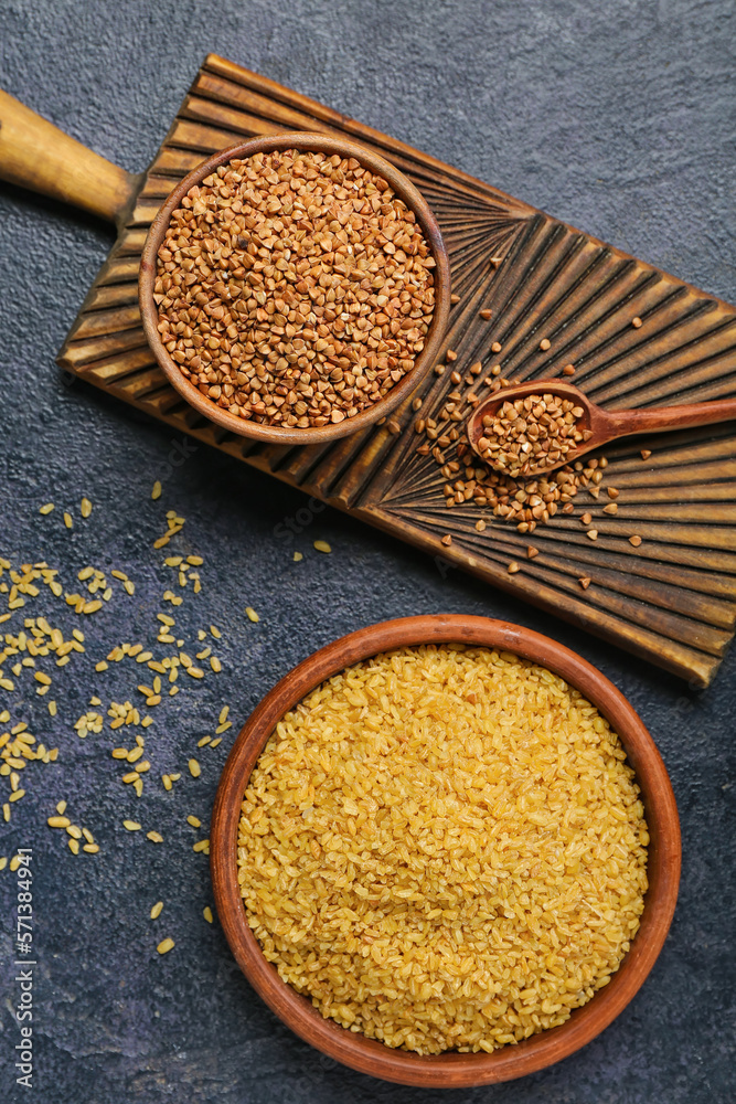 Bowls of buckwheat and bulgur on dark background