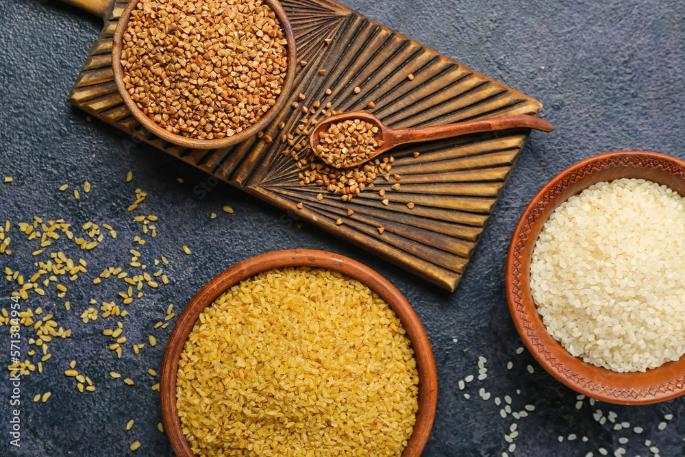 Bowls with buckwheat, rice and bulgur on dark background