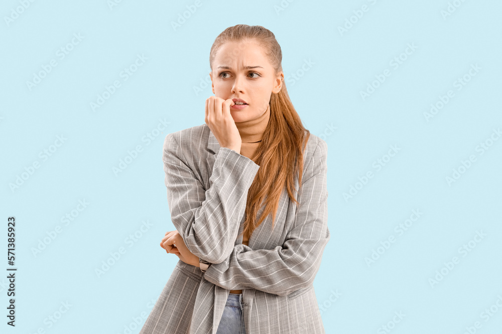 Young businesswoman biting nails on blue background