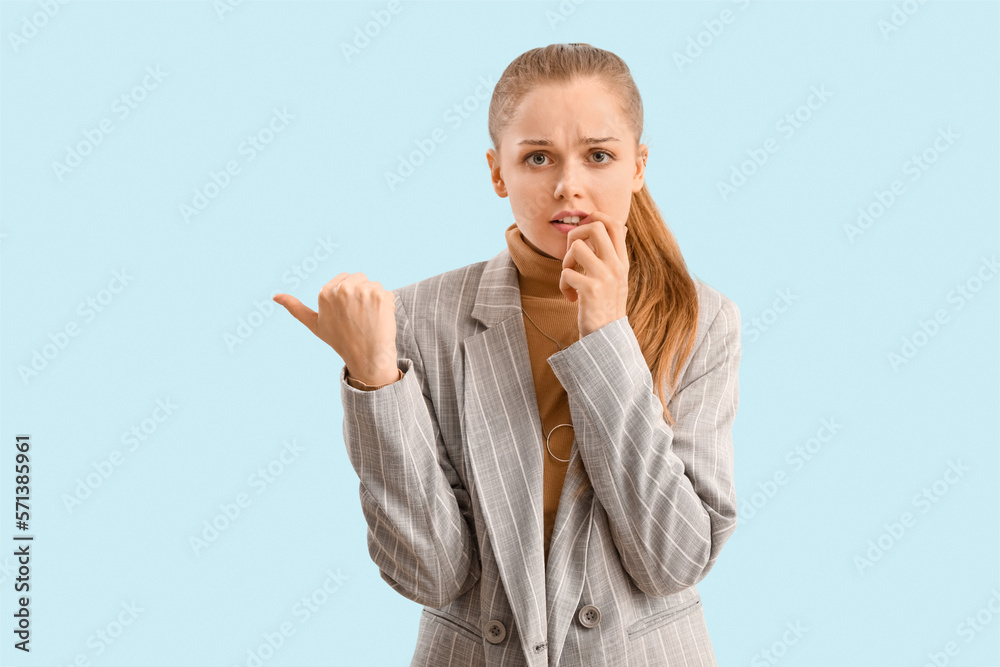 Young businesswoman biting nails and pointing at something on blue background