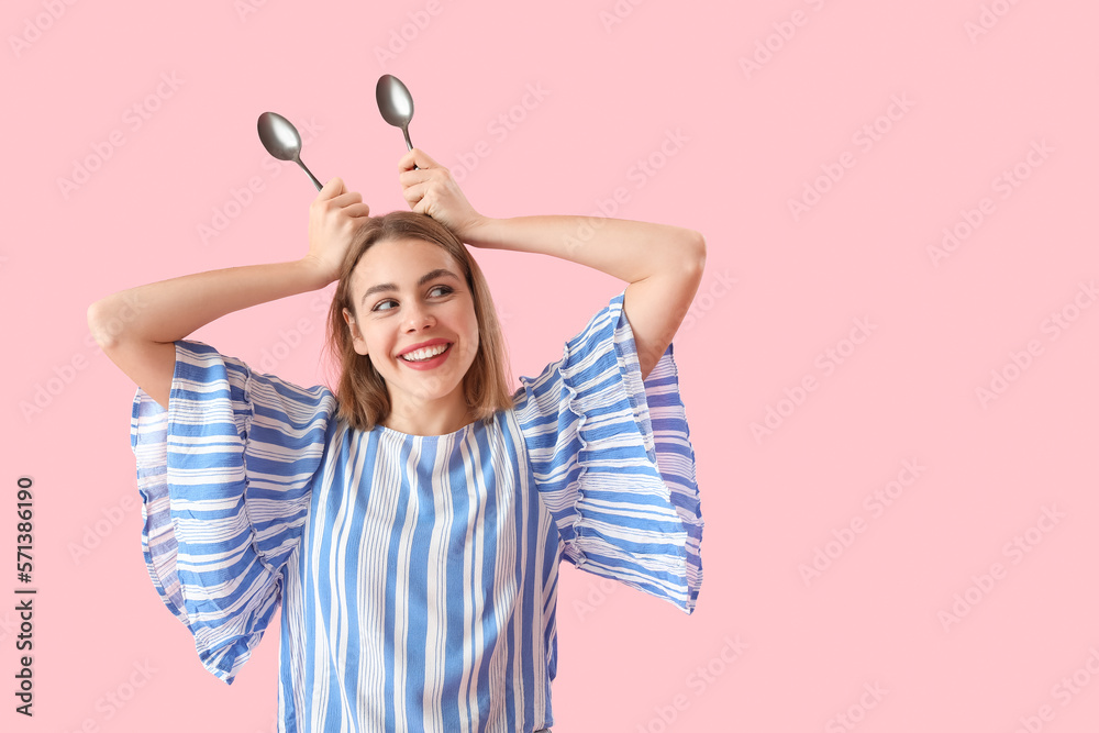 Funny young woman with spoons on pink background